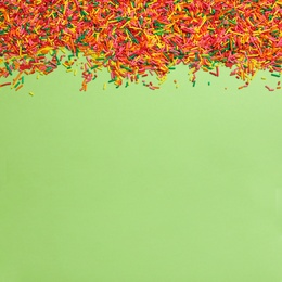 Photo of Colorful sprinkles on green background, flat lay with space for text. Confectionery decor