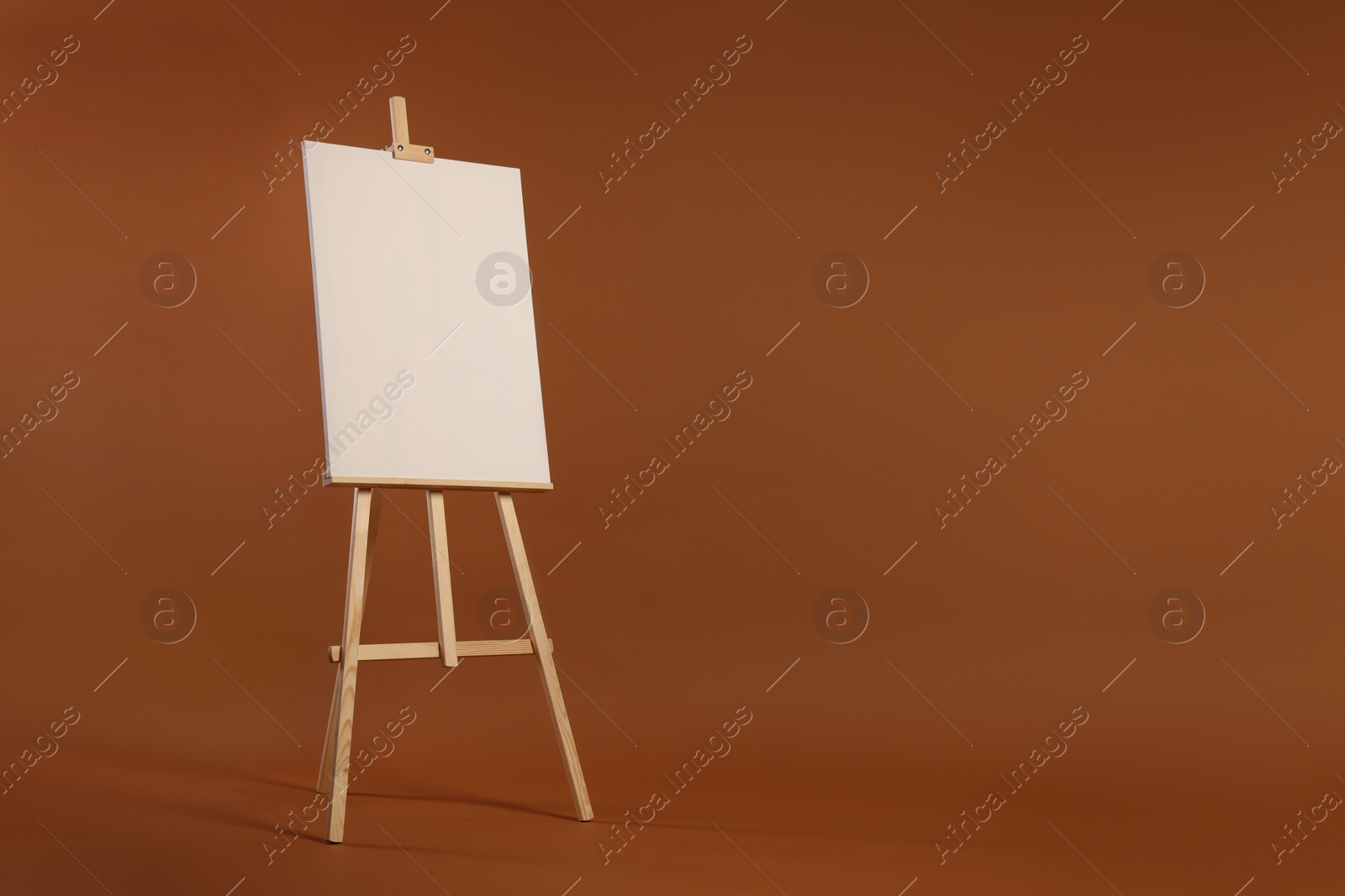 Photo of Wooden easel with blank canvas on brown background. Space for text