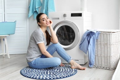 Photo of Young woman sitting near washing machine in laundry room