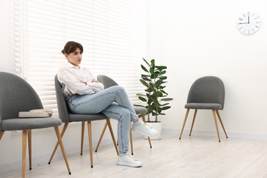 Photo of Woman sitting on chair and waiting for appointment indoors