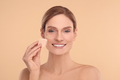 Photo of Woman blending foundation on face with makeup sponge against beige background