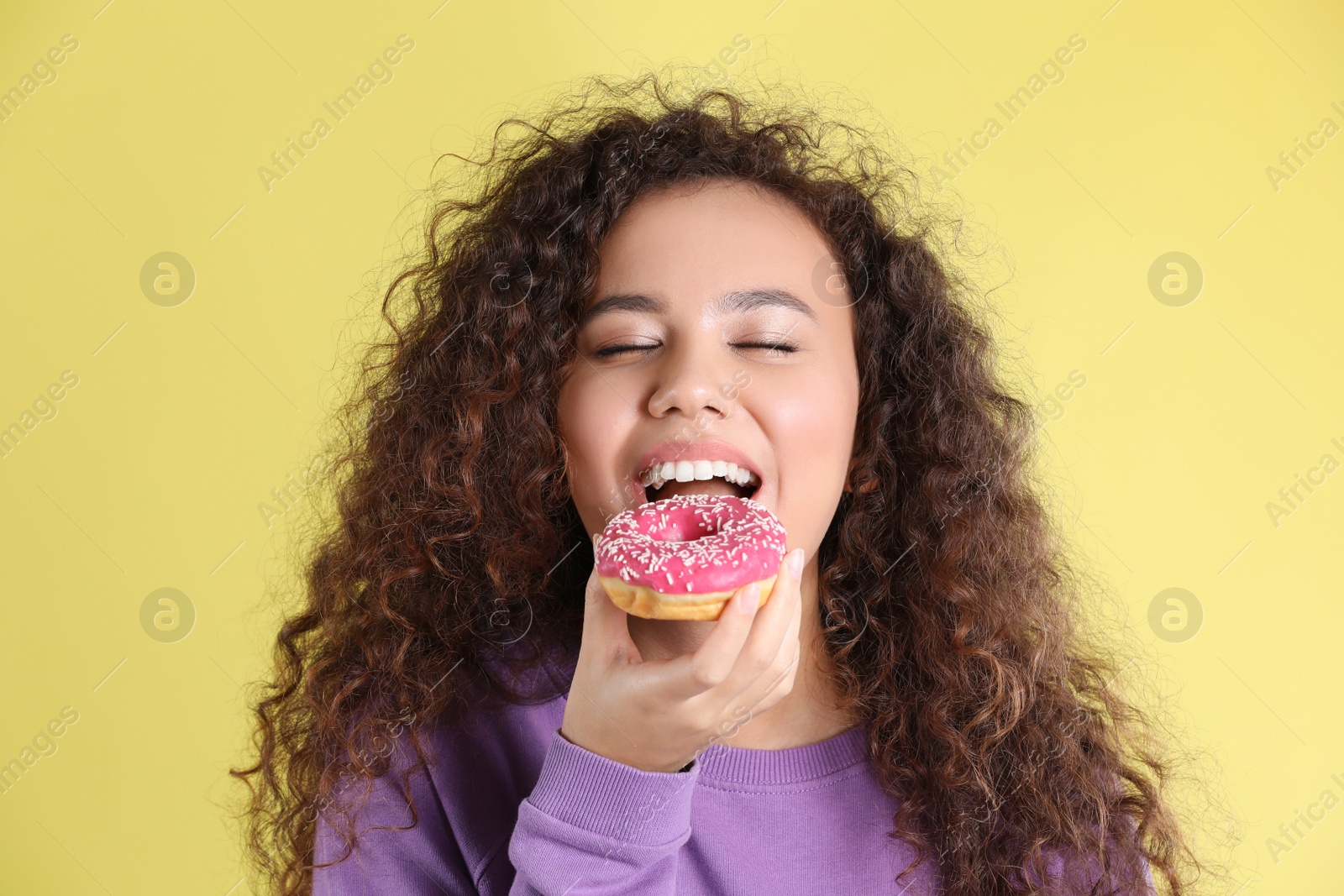 Photo of Beautiful African-American woman with donut on yellow background