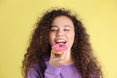 Photo of Beautiful African-American woman with donut on yellow background