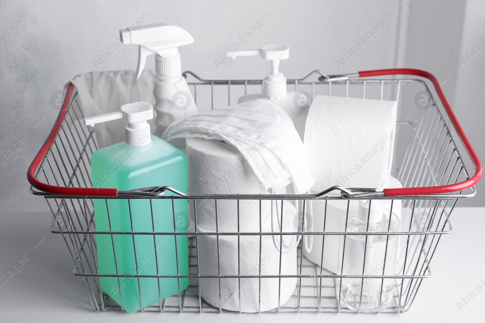 Photo of Shopping basket with antiseptics, toilet paper and masks on table indoors. Panic caused by virus