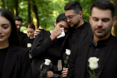 Funeral ceremony. Sad people with white rose flowers mourning outdoors
