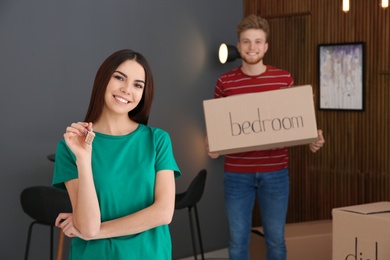 Photo of Young woman with key from new house and her boyfriend indoors. Moving day