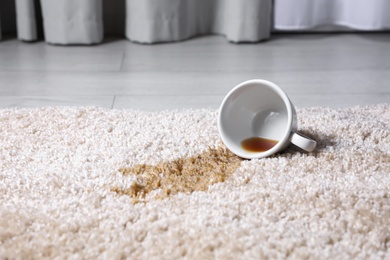 Photo of Overturned cup and spilled tea on beige carpet, closeup. Space for text