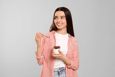 Photo of Happy teenage girl with delicious yogurt and spoon on light grey background