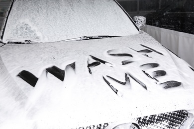 Photo of Inscription WASH ME on automobile covered with foam at car wash