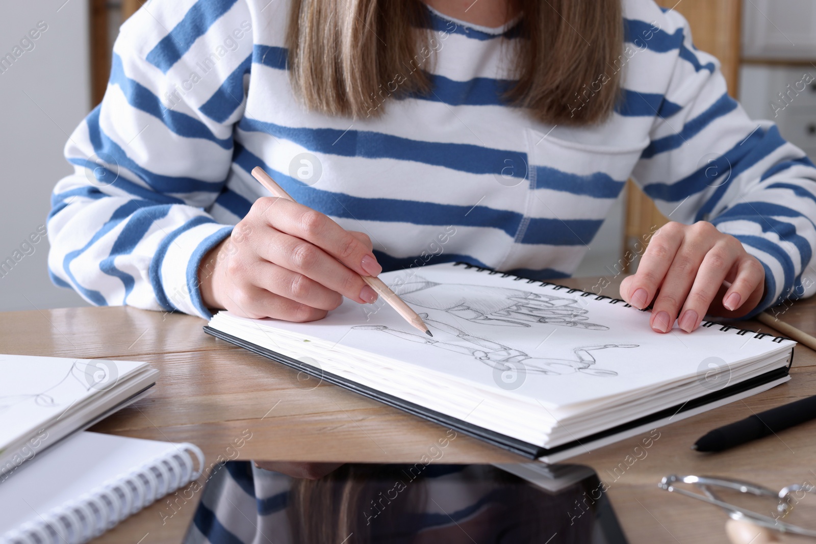 Photo of Woman drawing in sketchbook with pencil at wooden table, closeup