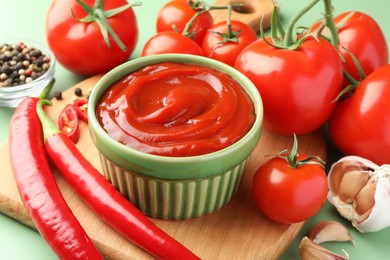 Photo of Bowl of tasty ketchup and ingredients on green table, closeup