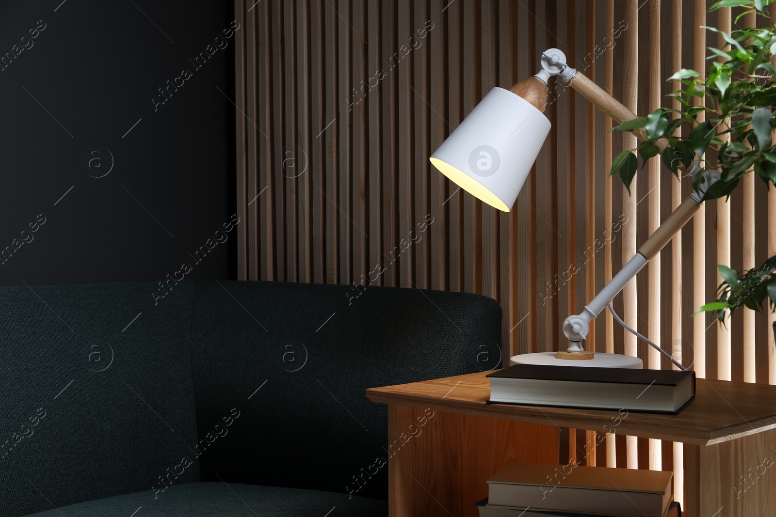 Photo of Stylish modern desk lamp and book on wooden cabinet in living room