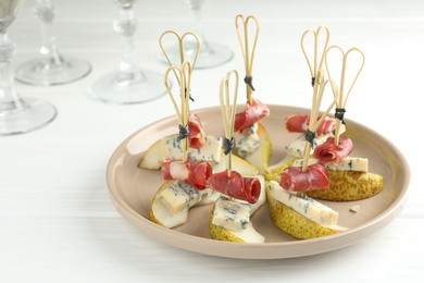 Tasty canapes with pears, blue cheese and prosciutto on white wooden table, closeup