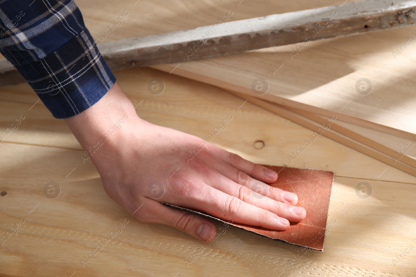 Photo of Man polishing wooden planks with sandpaper, closeup