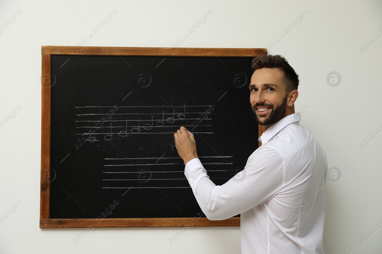 Photo of Teacher writing music notes with chalk on blackboard in classroom