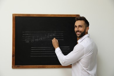 Teacher writing music notes with chalk on blackboard in classroom