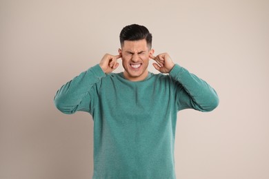 Photo of Emotional man covering ears with fingers on beige background