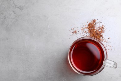 Photo of Freshly brewed rooibos tea and scattered dry leaves on grey table, flat lay. Space for text