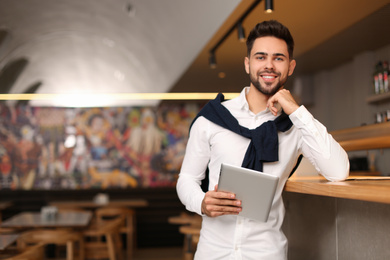 Photo of Young male business owner with tablet near counter in his cafe. Space for text