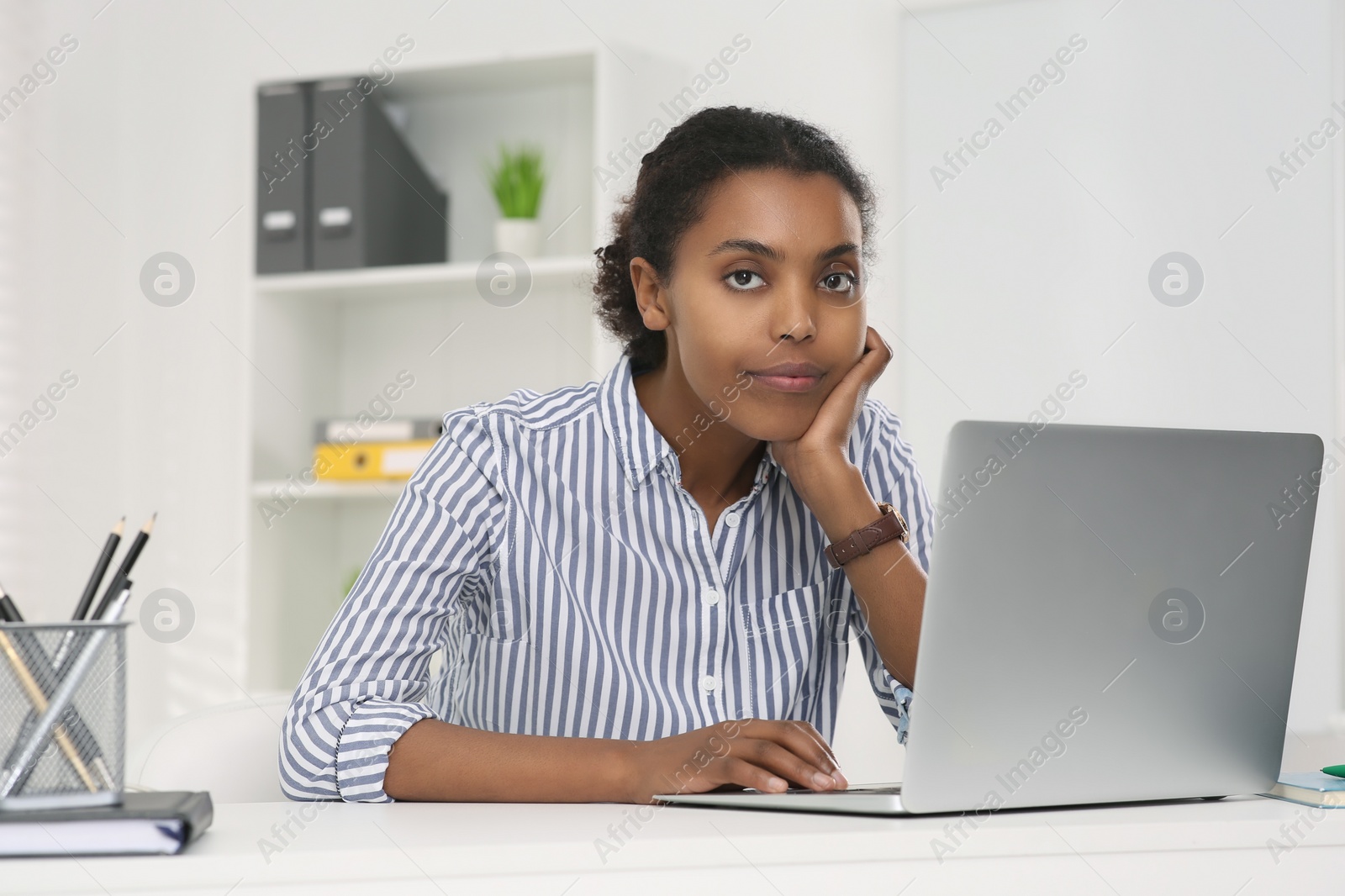 Photo of Sad African American intern working on laptop at white table in office. First work day