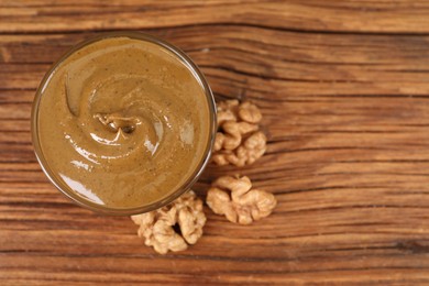 Delicious nut butter in bowl and walnuts on wooden table, top view. Space for text