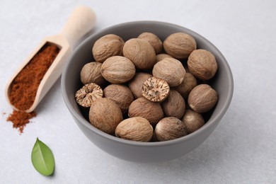 Photo of Nutmegs in bowl and scoop with powder on light table, closeup