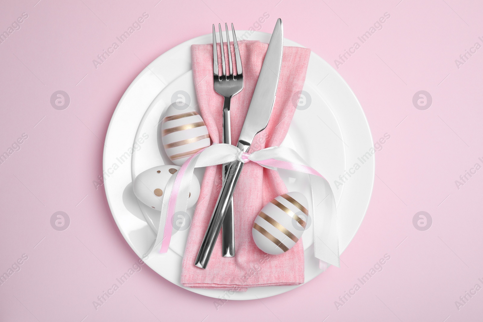 Photo of Festive table setting with painted eggs and cutlery on pink background, top view. Easter celebration