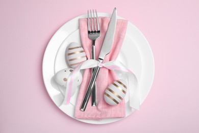 Photo of Festive table setting with painted eggs and cutlery on pink background, top view. Easter celebration