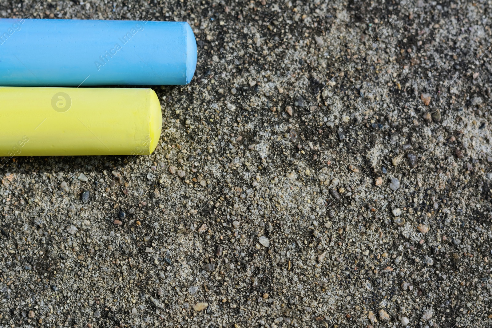 Photo of Yellow and light blue chalk sticks on asphalt, flat lay. Space for text