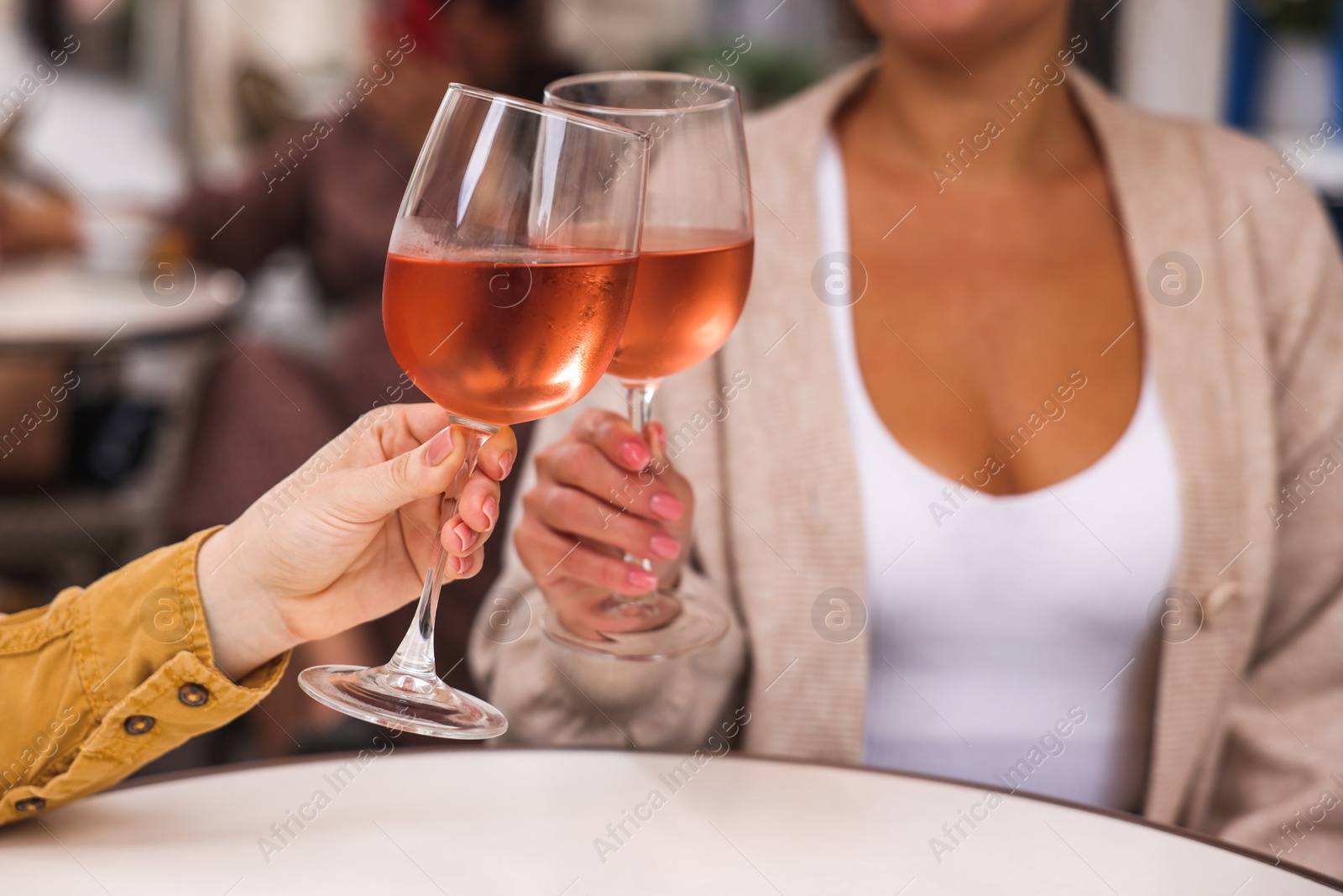 Photo of Women clinking glasses with rose wine at white table in outdoor cafe, closeup