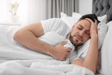 Man suffering from headache while lying on bed at home