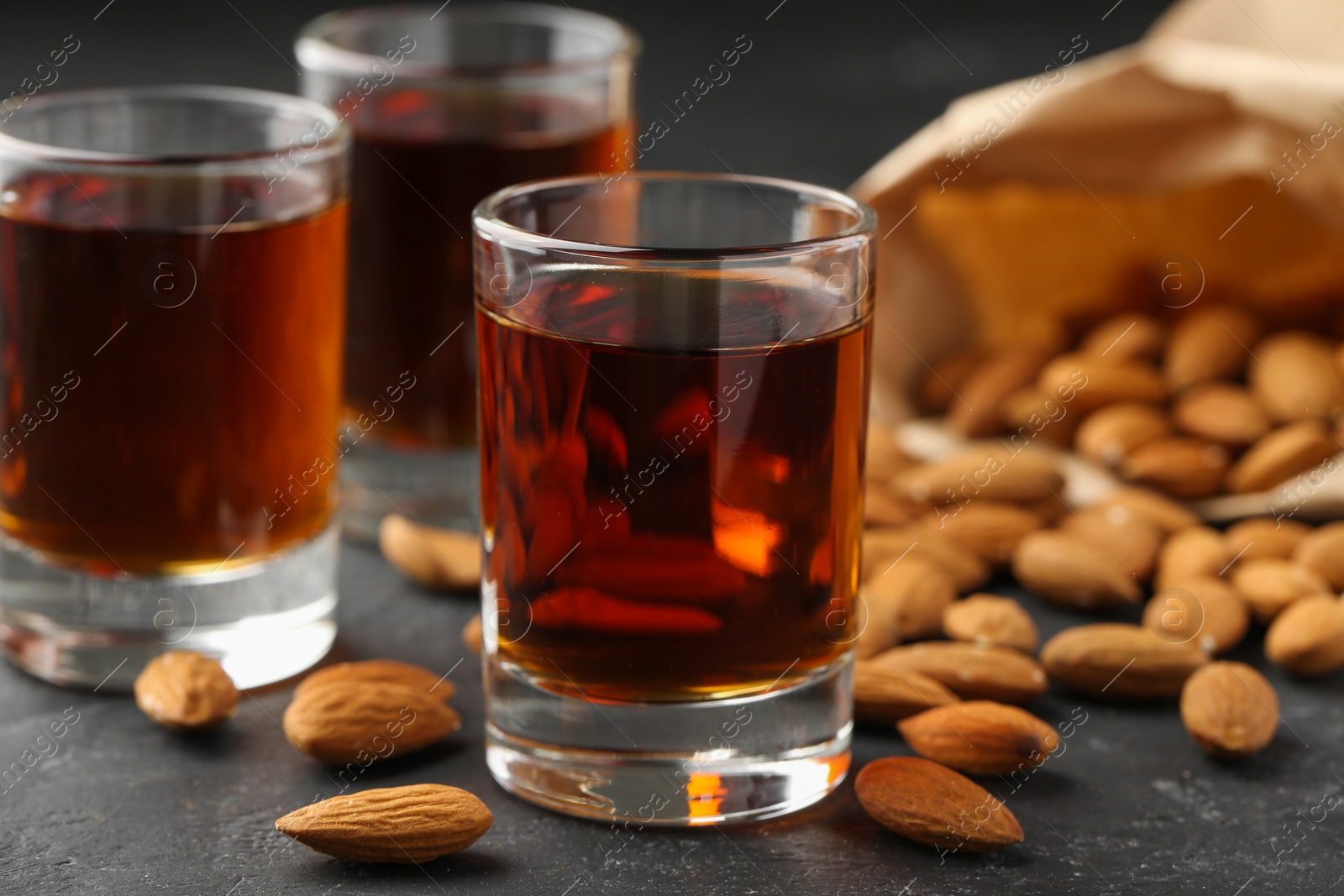 Photo of Glasses with tasty amaretto liqueur and almonds on dark gray table, closeup