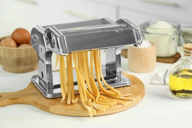 Photo of Pasta maker with raw dough and ingredients on white wooden table