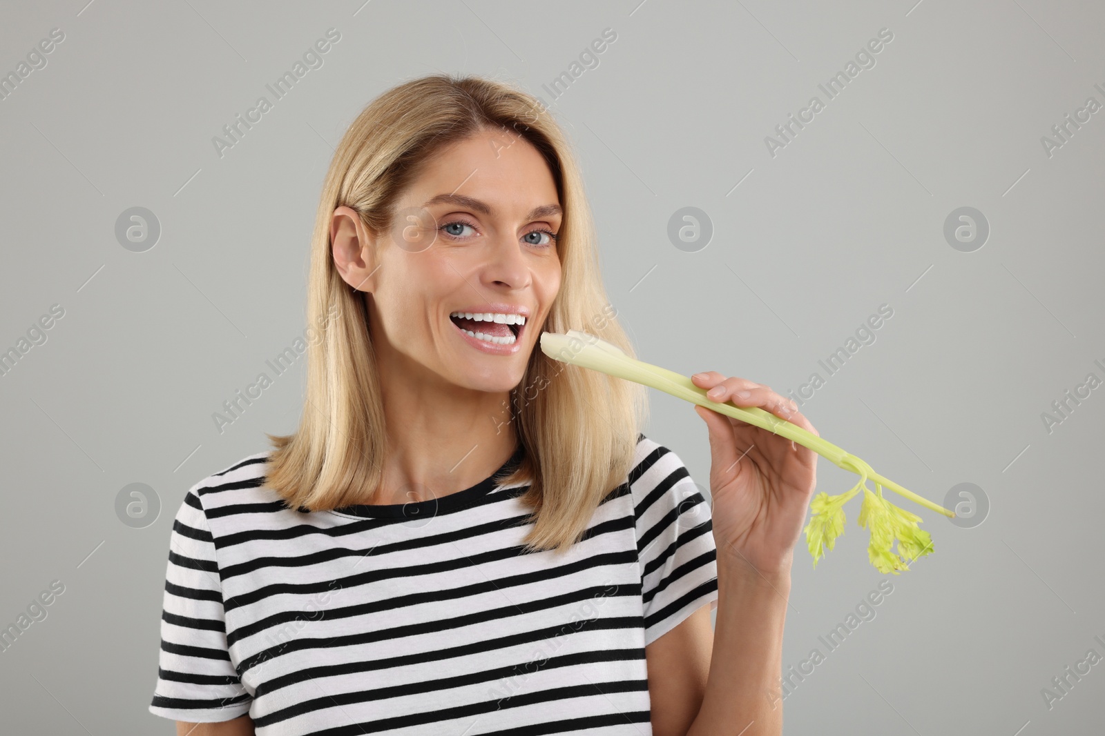 Photo of Woman with fresh green celery stem on light grey background