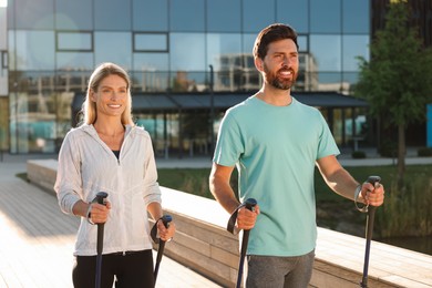 Photo of Happy couple practicing Nordic walking with poles outdoors