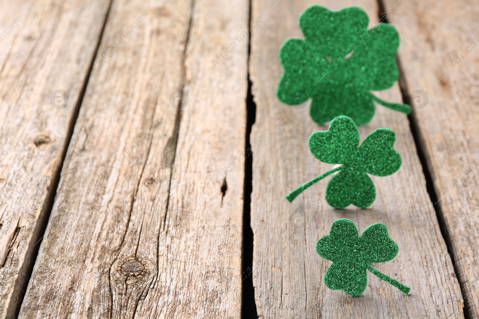 Photo of St. Patrick's day. Shiny decorative clover leaves on wooden table, selective focus. Space for text