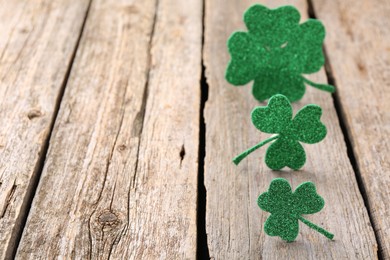 Photo of St. Patrick's day. Shiny decorative clover leaves on wooden table, selective focus. Space for text