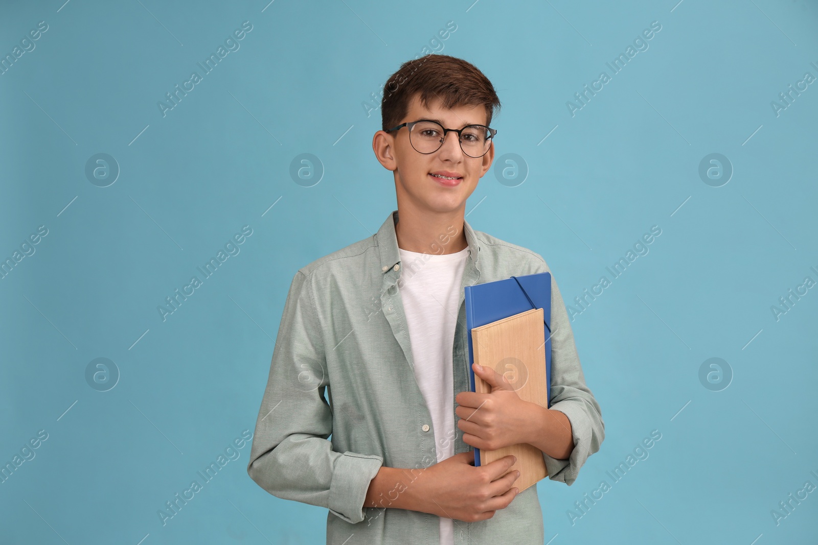 Photo of Teenage student with glasses and stationery on turquoise background