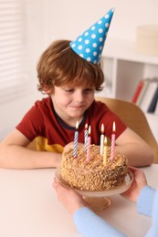 Photo of Birthday celebration. Mother holding tasty cake with burning candles near her son indoors