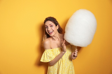 Portrait of young woman with cotton candy on yellow background