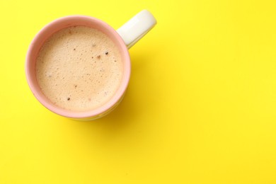 Photo of Aromatic coffee in cup on yellow background, top view. Space for text