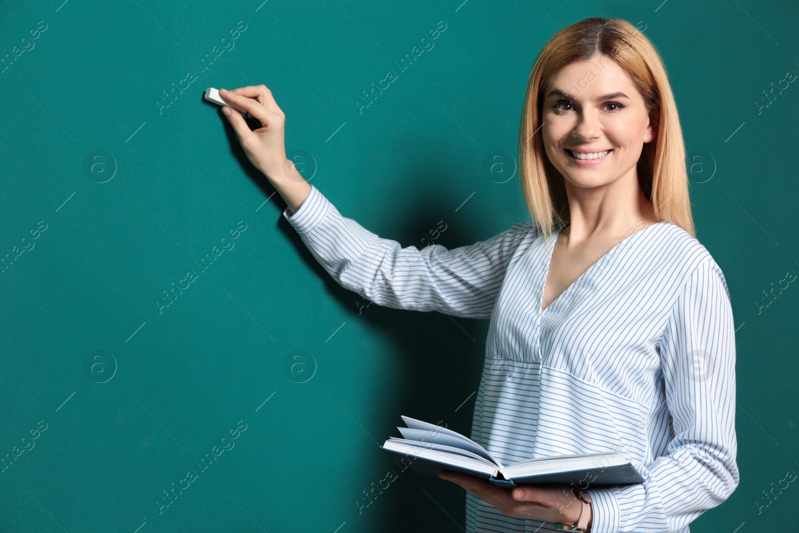 Photo of Beautiful teacher with book writing on chalkboard, space for text