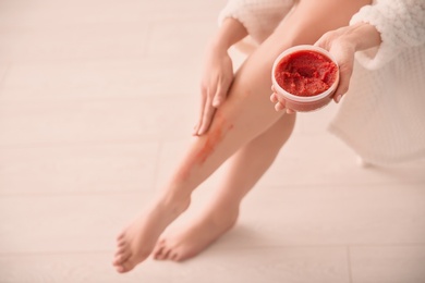 Woman applying body scrub on legs at home