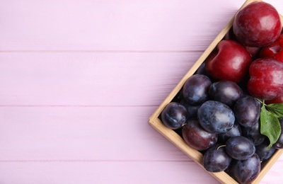 Delicious ripe plums in crate on pink wooden table, top view. Space for text