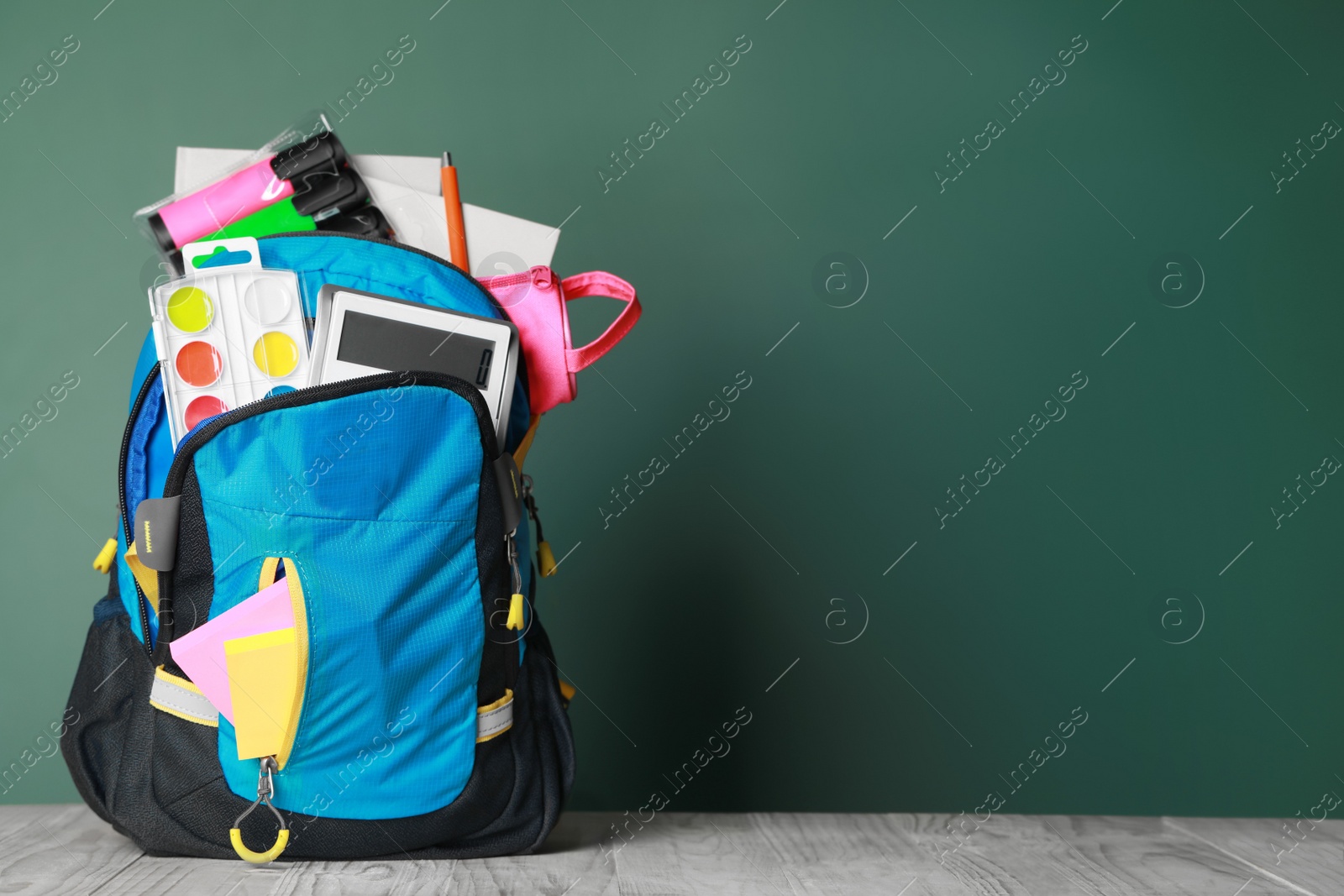 Photo of Backpack with different school stationery on wooden table near chalkboard, space for text