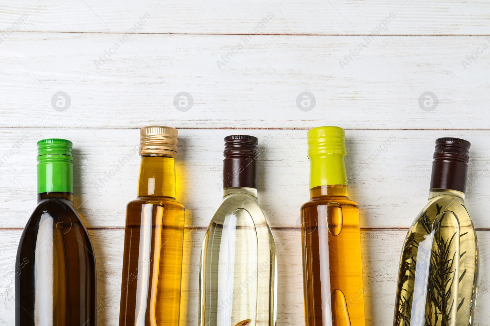 Photo of Different sorts of cooking oil in bottles on white wooden table, flat lay