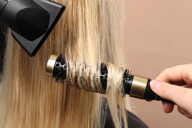 Photo of Hairdresser blow drying client's hair on beige background, closeup