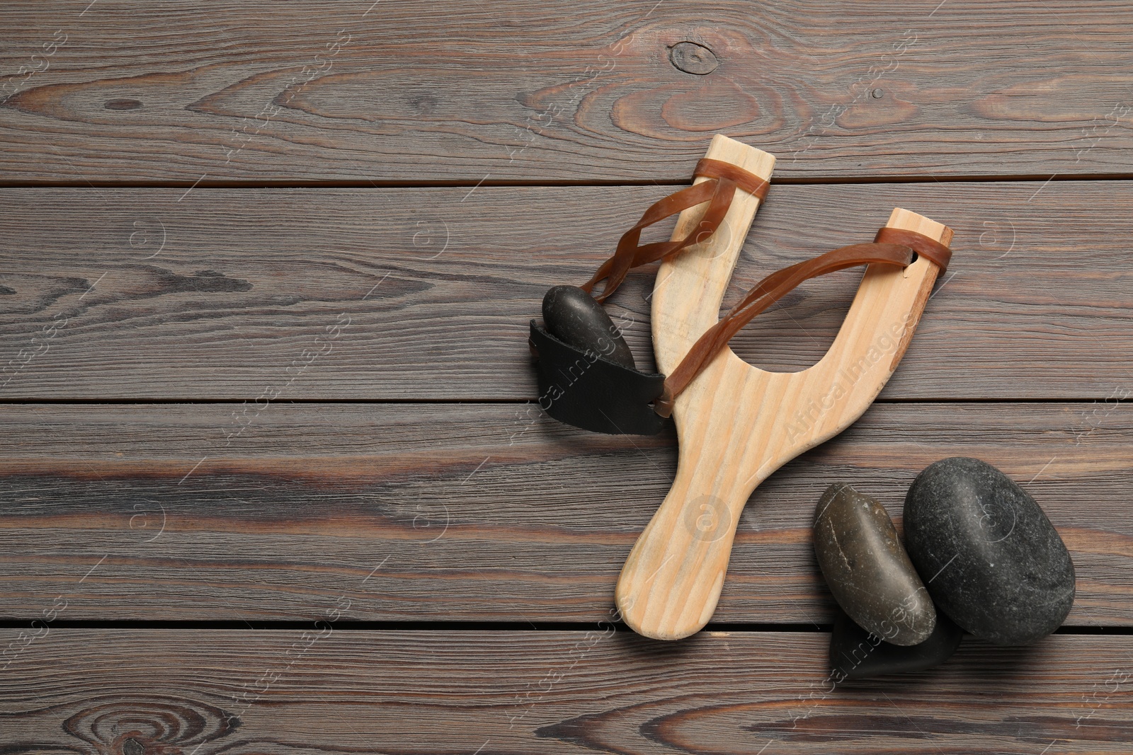 Photo of Slingshot with stones on wooden background, flat lay. Space for text