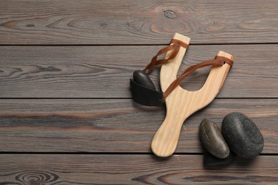 Slingshot with stones on wooden background, flat lay. Space for text