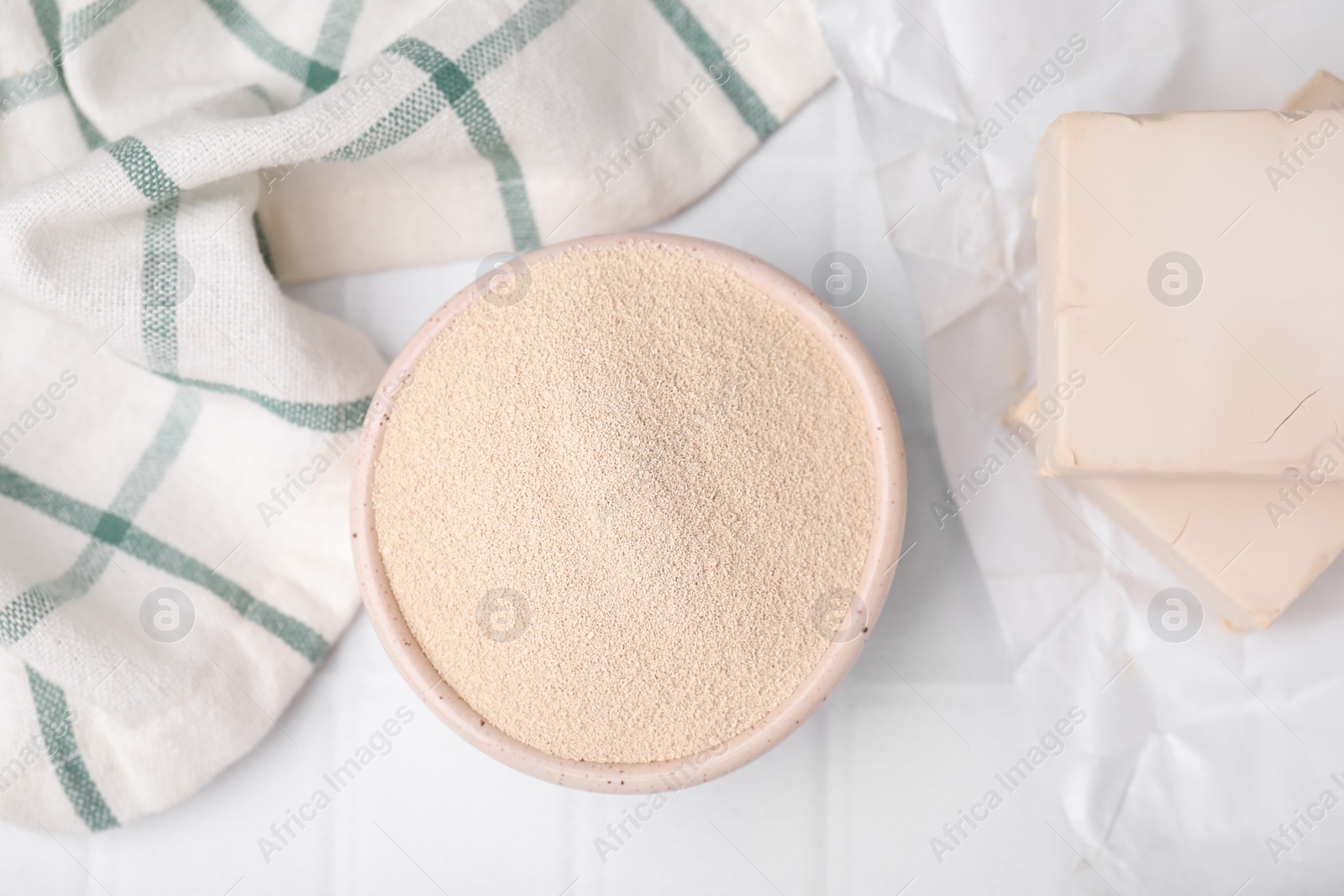 Photo of Granulated and compressed yeast in bowl on white tiled table, flat lay